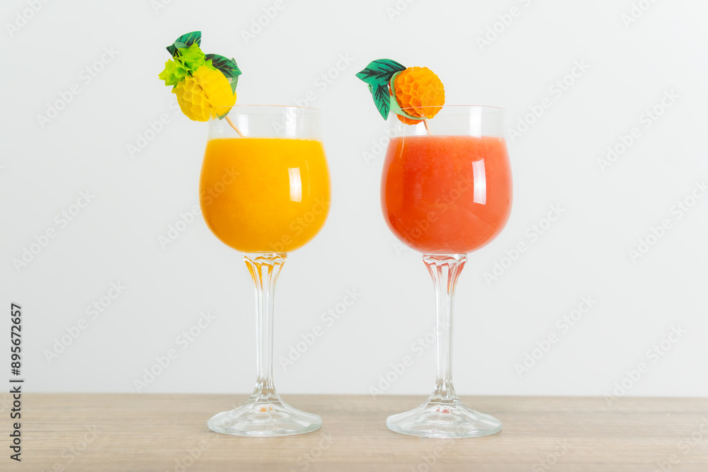 two Hawaiian cocktails of fruits and alcohol in decorated crystal glasses, one orange and one red on a wooden bar and a white background. Concept: photo for Bar or Cafeteria decoration. two Hawaiian cocktails of fruits and alcohol in decorated crystal glasses, one orange and one red on a wooden bar and a white background. Concept: photo for Bar or Cafeteria decoration.