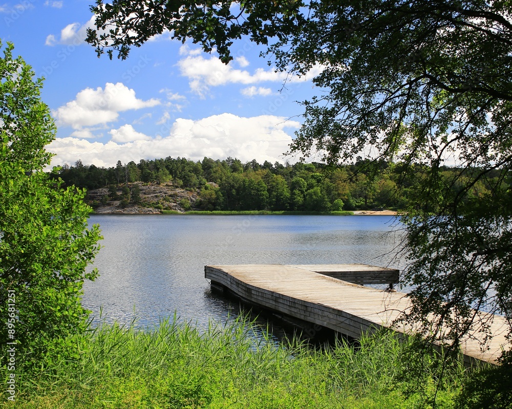 View over Brunnsviken bay, Stockholm, with wooden pier and lush greenery on a clear summer day