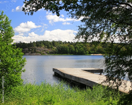 View over Brunnsviken bay, Stockholm, with wooden pier and lush greenery on a clear summer day photo