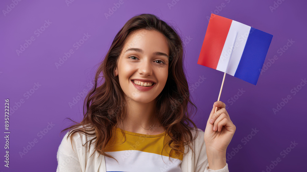 A smiling student holding a small French flag, set against a purple background, representing her dedication to learning French. A smiling student holding a small French flag, set against a purple background, representing her dedication to learning French.