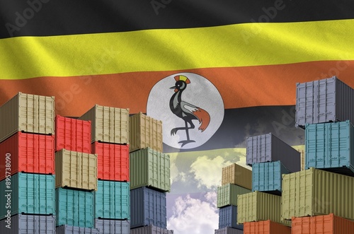 Uganda flag and big stack of shipping cargo containers in docks with sky background close up photo