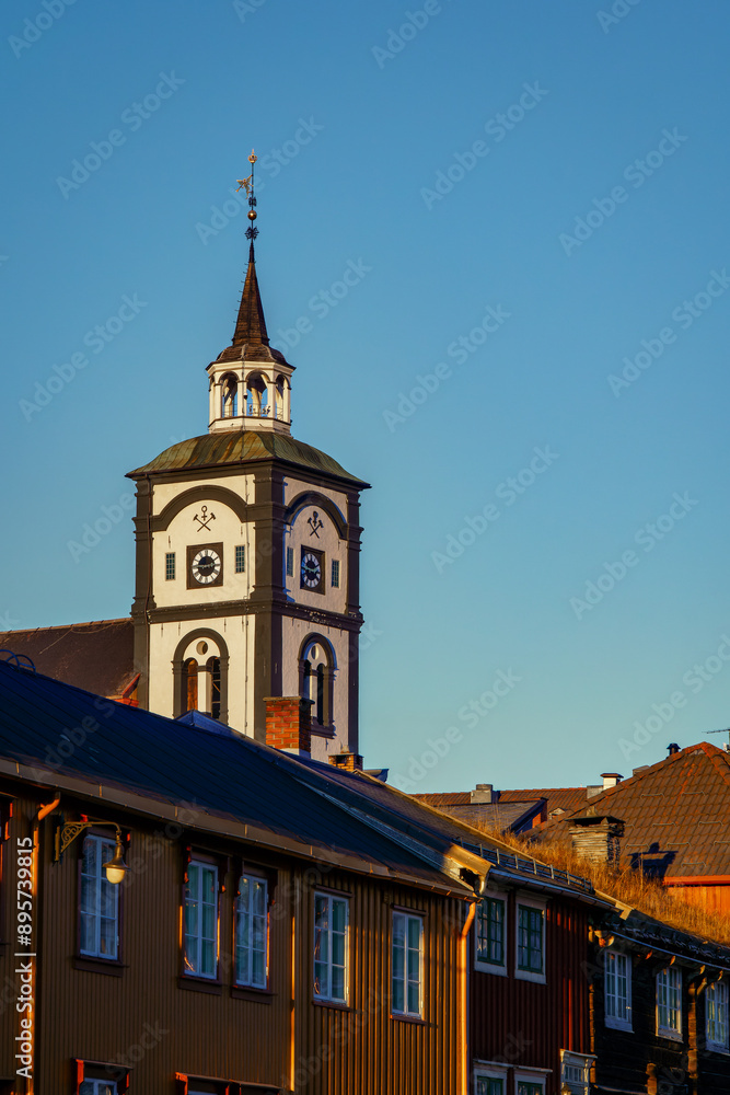 Naklejka premium Sunset rays illuminate the charming landscape of Roros, featuring the town's landmark church and wooden architecture