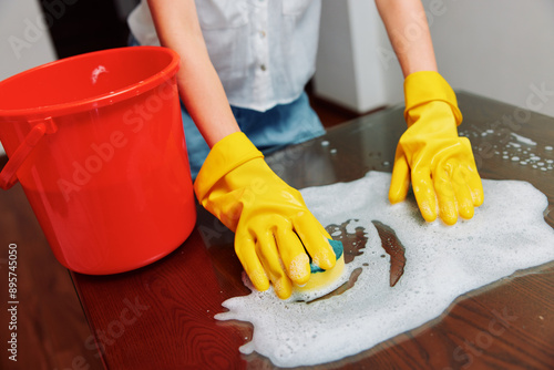 Woman in rubber gloves cleaning a table with soap and water buckets photo