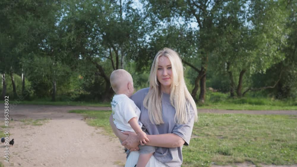 A beautiful young mother with a small child in her arms walks in the park in summer A beautiful young mother with a small child in her arms walks in the park in summer