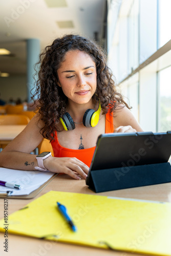 Young curly haired girl smiling using tablet in university library