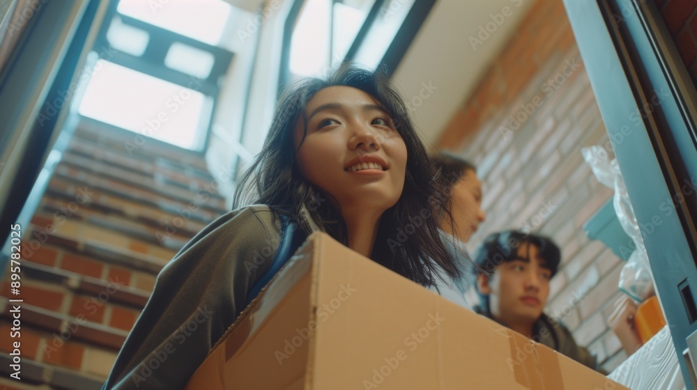 A woman holds a box against a brick wall, possibly moving or storing something A woman holds a box against a brick wall, possibly moving or storing something