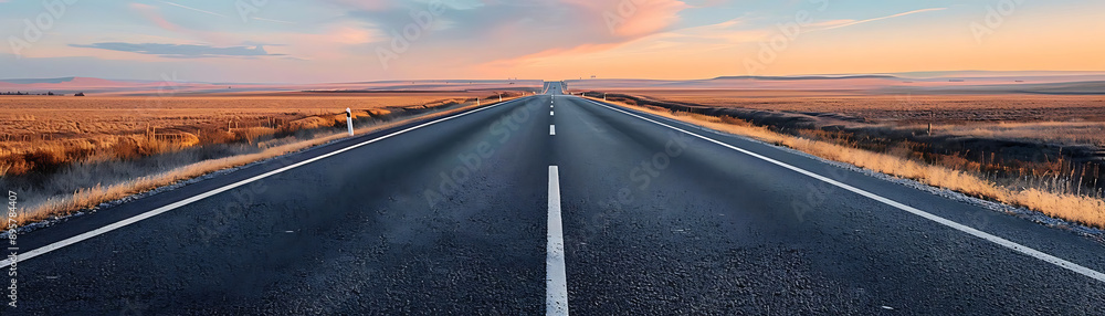 Fototapeta premium A serene landscape featuring an empty road stretching into the horizon under a colorful sunset sky.