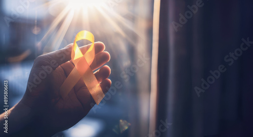 Close-up of a hand holding a yellow ribbon with rays of sunlight symbolizing support, awareness, and Suicide Prevention Day photo