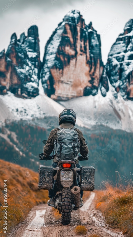 Image of person in motorcycle gear on a dirt road, mountains in the background. Bike with mud-covered storage box hints at journey through natural landscape. Image of person in motorcycle gear on a dirt road, mountains in the background. Bike with mud-covered storage box hints at journey through natural landscape.