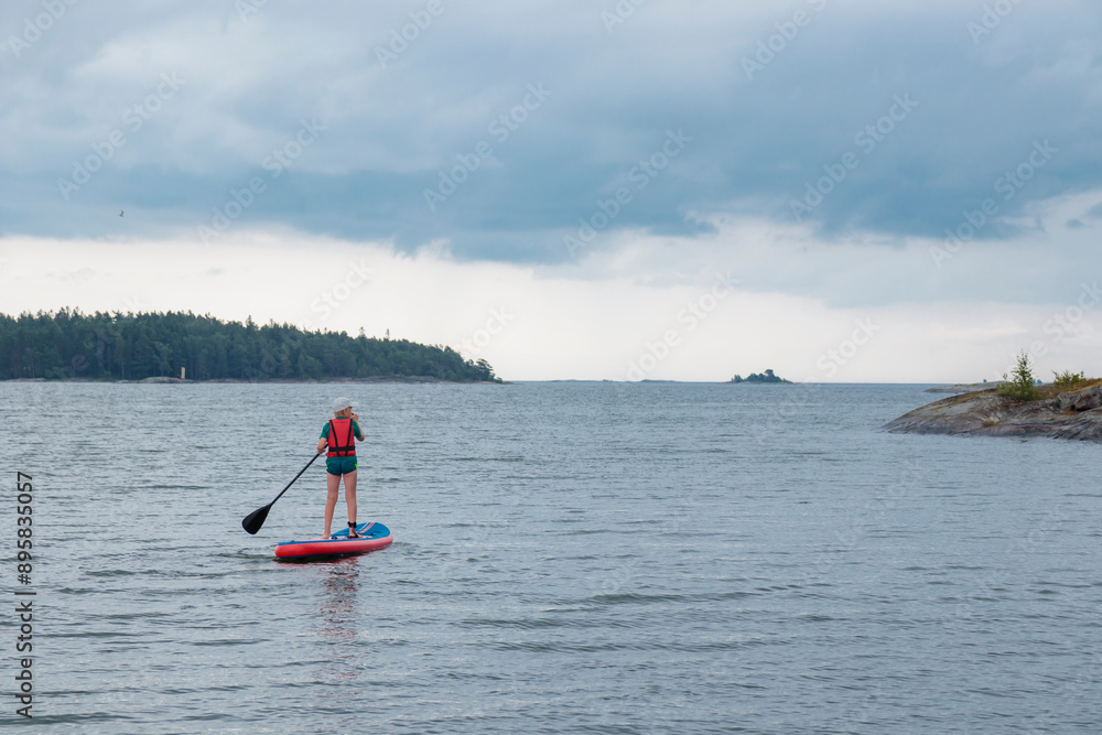 Naklejka premium Little boy paddling on a paddle surfboard sup board in Baltic sea, Gulf of Finland, kids vacation, summer holidays in Finland