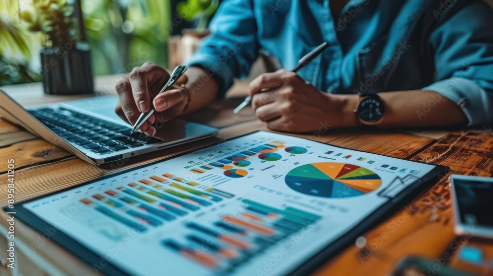 Close-up of a person's hands analyzing financial data on a laptop and charts. Close-up of a person's hands analyzing financial data on a laptop and charts.