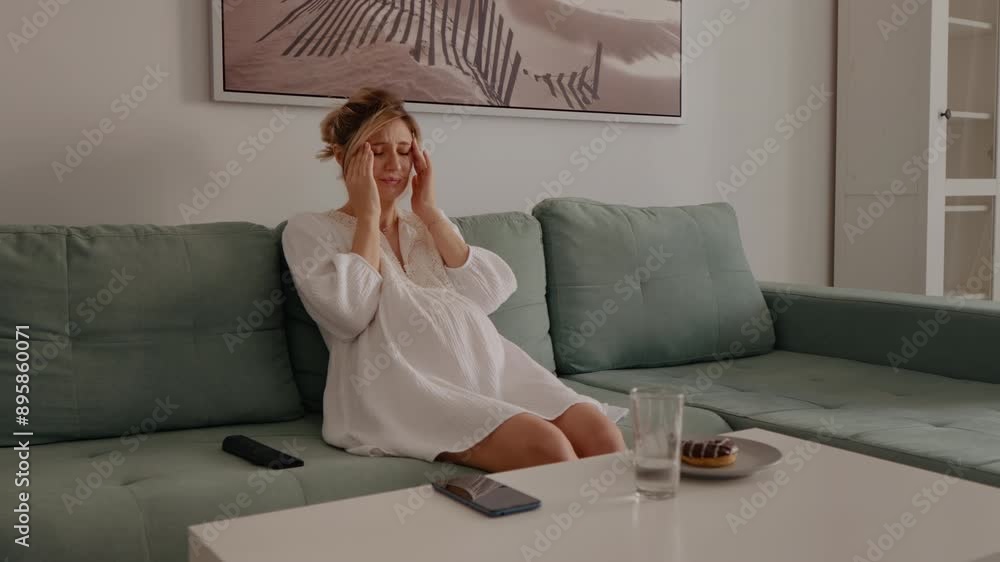 Pregnant woman sitting on sofa suffering for headache at home massaging her temples. Future parent female feeling sick with hurting head. Lady in maternity massage herself Pregnant woman sitting on sofa suffering for headache at home massaging her temples. Future parent female feeling sick with hurting head. Lady in maternity massage herself