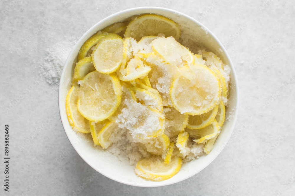 Overhead view of lemon slices and sugar being mixed together in a white bowl, process of making lemon cheong or lemon syrup Overhead view of lemon slices and sugar being mixed together in a white bowl, process of making lemon cheong or lemon syrup