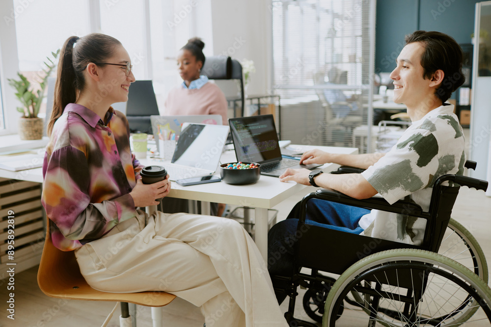 Young Caucasian female colleague holding cup of coffee and chatting lovely with her Caucasian male colleague with disability Young Caucasian female colleague holding cup of coffee and chatting lovely with her Caucasian male colleague with disability