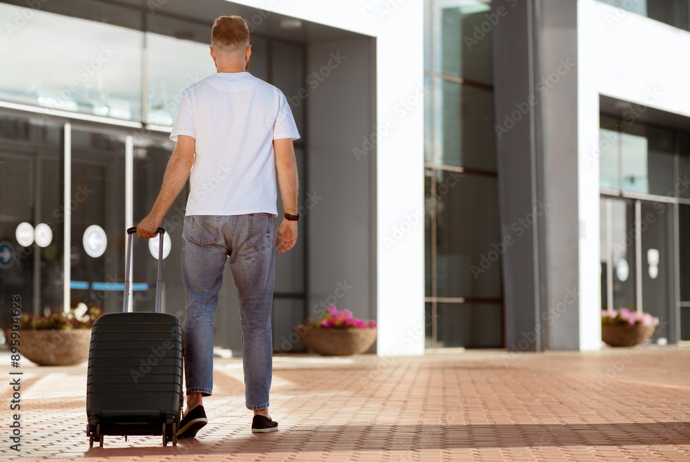 Vacation Time Concept. Caucasian man carrying suitcase and walking to airport terminal, view from the back, copyspace