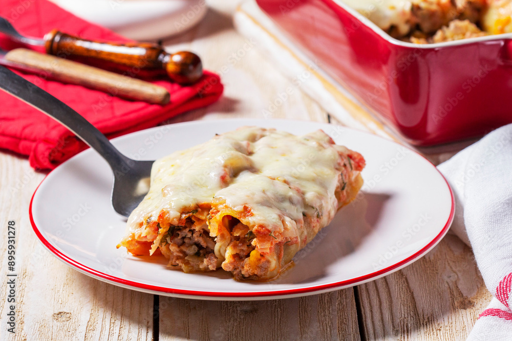 Cannellone with meat filling, tomato sauce and cheese on a light wooden table.
