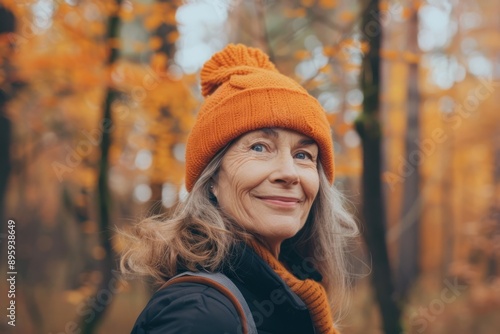 Positive cheerful woman in orange hat enjoying walk outdoors in autumn forest. Happy older woman