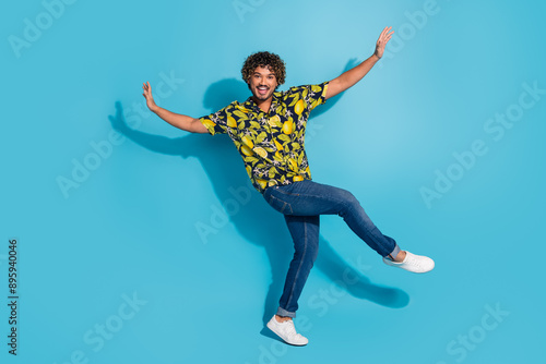 Full size photo of optimistic eccentric man dressed print shirt jeans raising arms up dancing having fun isolated on blue color background © deagreez