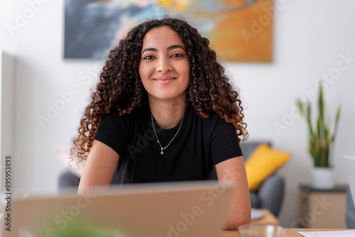 A woman wearing headphones and using a smartphone while working on a laptop. This image showcases a focused and modern workspace, integrating technology for efficiency. photo