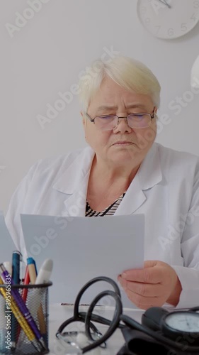 Vertical Screen: Female doctor analysing paperboard report tired taking her glasses of. Tired docor needs a rest. Medicare concept. photo