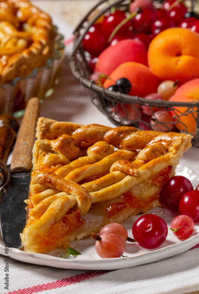 Apricot pie decorated with dough ornament and a metal basket with fruits and berries.