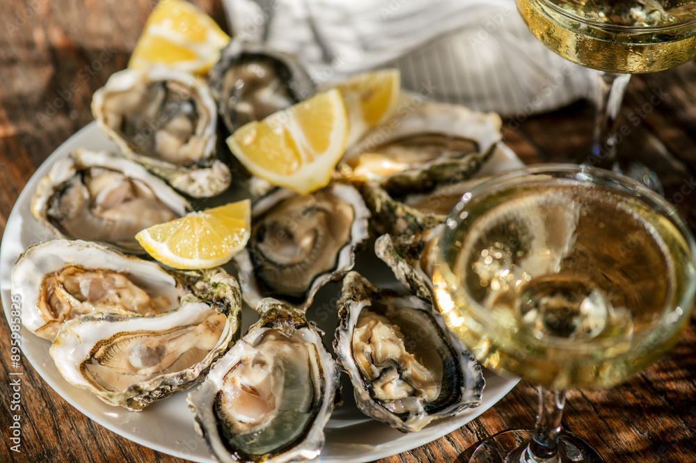 Fresh Oysters with champagne close up top view, over wood background, open french Fine de Claire oysters. Dinner in a restaurant, sea food. Served table with Oyster. Gourmet food, delicatessen. Fresh Oysters with champagne close up top view, over wood background, open french Fine de Claire oysters. Dinner in a restaurant, sea food. Served table with Oyster. Gourmet food, delicatessen.