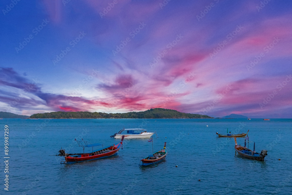 Naklejka premium Colourful Skies Sunset over Rawai Beach in Phuket island Thailand. Lovely turquoise blue waters, lush green mountains colourful skies and beautiful views of long tail Boats