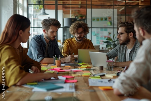 A team of professionals is engaged in a collaborative meeting with laptops and colorful sticky notes on the table, embodying innovation and teamwork in a lively workspace.