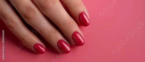 Woman's hand with dark pink/red nails on pink background exudes gentleness and romance, emphasizing harmony between manicure color and background.