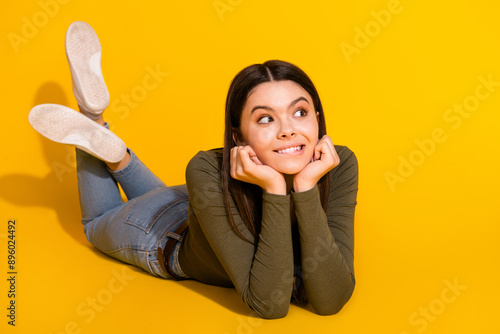 Full size photo of pretty teenager girl look empty space interested lying wear trendy khaki outfit isolated on yellow color background photo