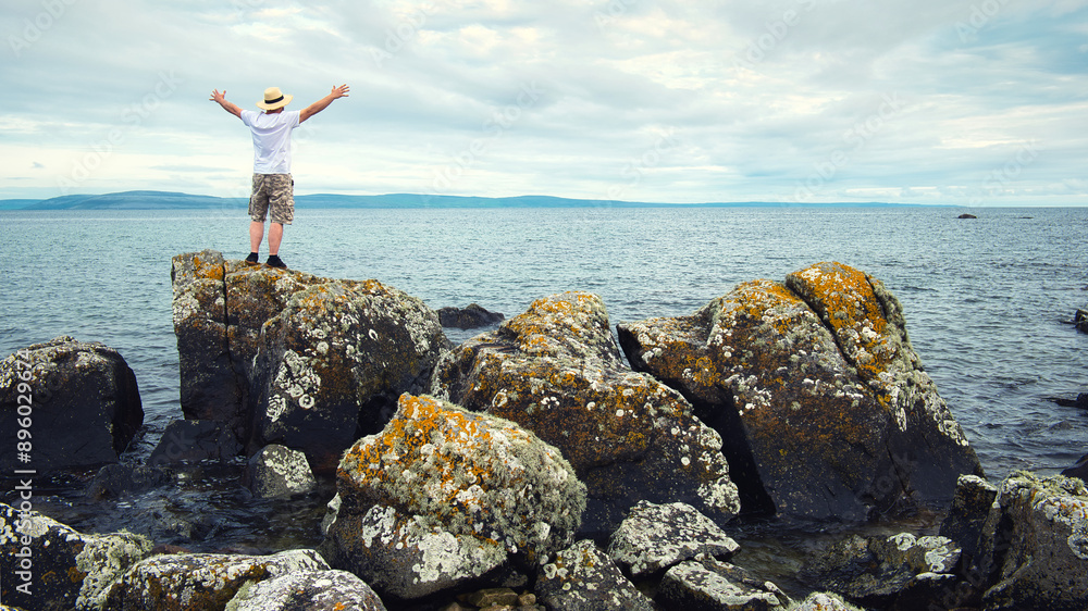 Handsome bearded man with straw hat standing on the rocks by the ocean at wild Atlantic way, adventure and lifestyle concept, summer, vacation, nature background