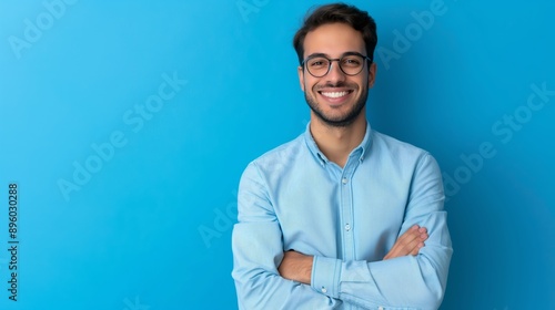 A man with glasses is smiling and standing in front of a blue wall. He is wearing a blue shirt and has his arms crossed © Nataliia_Trushchenko