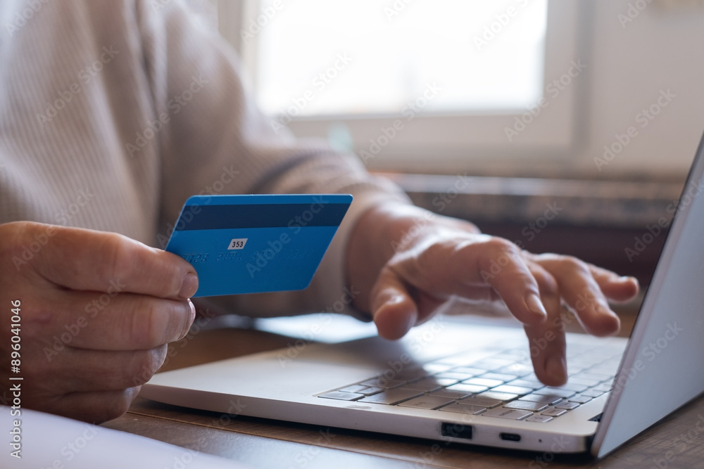 Fototapeta premium A woman is making an online purchase or payment, utilizing card and a laptop 