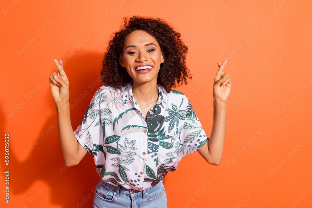 Photo of american young positive girl with curly hair in summer shirt keeping balance crossed fingers isolated on orange color background Photo of american young positive girl with curly hair in summer shirt keeping balance crossed fingers isolated on orange color background