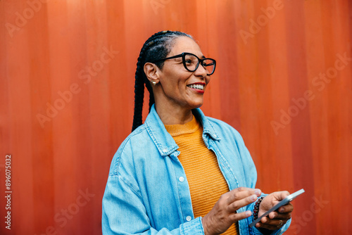 Fényképezés Latin American businesswoman using smartphone in vibrant setting