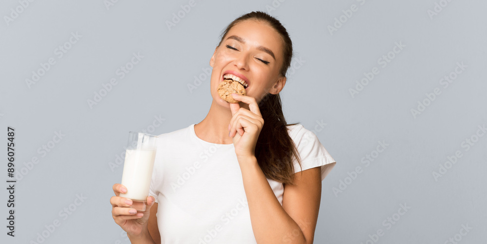 Millennial Girl Drinking Glass Of Milk And Eating Cookies Standing Over Gray Studio Background. Panorama Millennial Girl Drinking Glass Of Milk And Eating Cookies Standing Over Gray Studio Background. Panorama