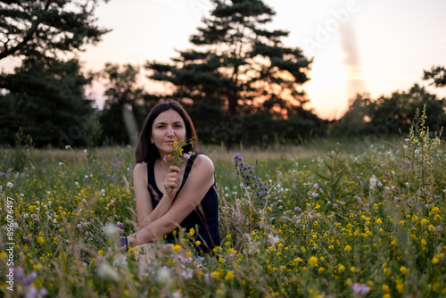 Beautiful young dreamy girl is sitting in nature and holding a bouquet of wildflowers