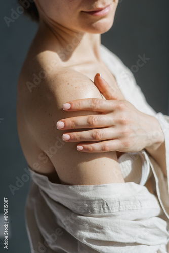 Woman in linen robe stands with her bare shoulder facing the camera