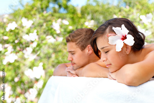 Massage, peace and couple at outdoor spa for skincare, health or relax for wellness on table. Calm, man and woman at luxury salon with hibiscus flower in nature for beauty therapy on holiday together