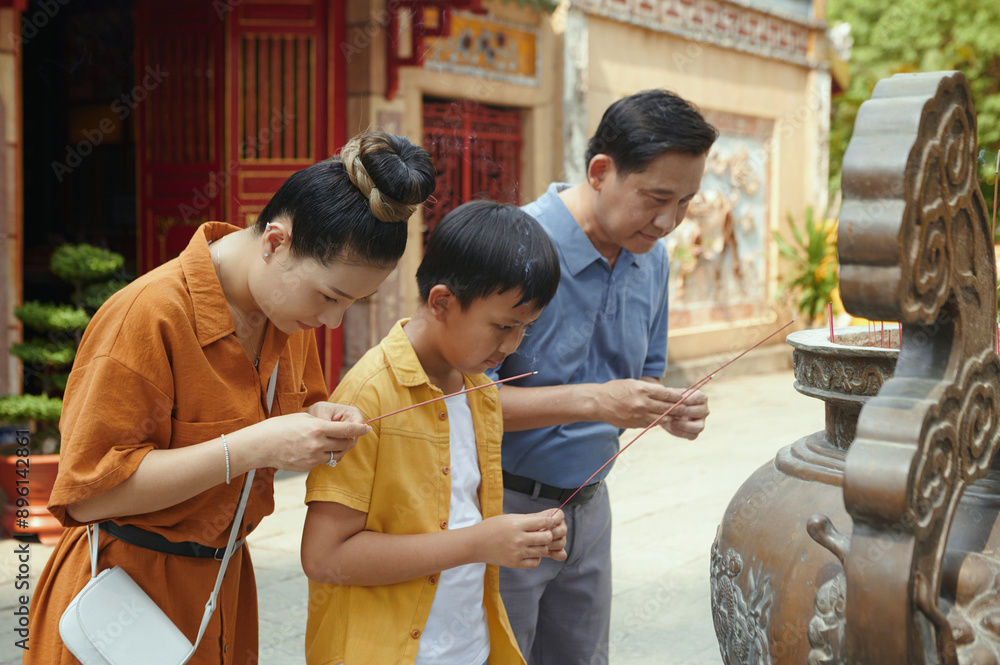 Fototapeta premium Family of three using aroma sticks while praying near the ancient sculpture