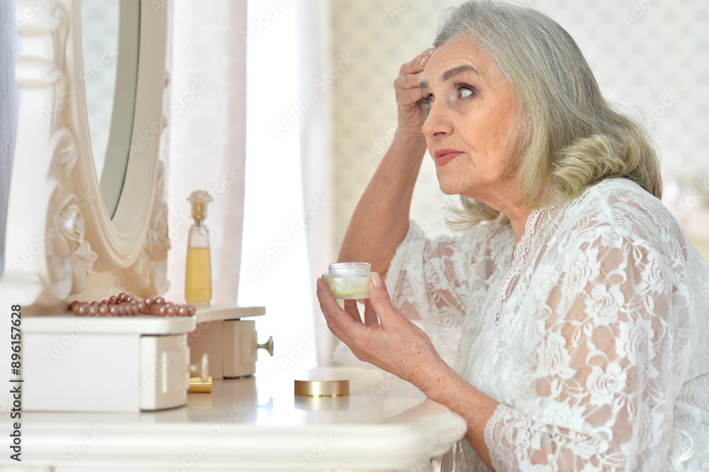 Smiling senior woman doing makeup in front of mirror at home Smiling senior woman doing makeup in front of mirror at home