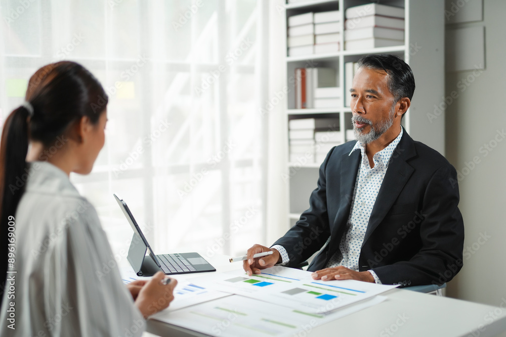 Senior executive gestures towards an analytics report while discussing a business strategy with a coworker Senior executive gestures towards an analytics report while discussing a business strategy with a coworker