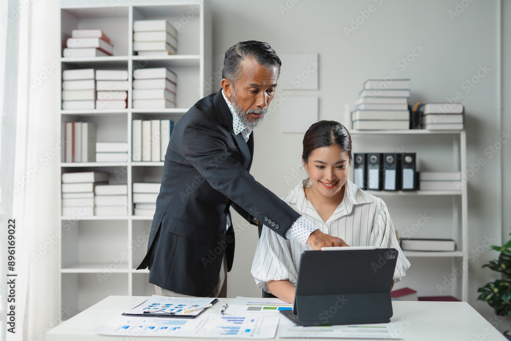 Senior manager demonstrating business strategy on digital tablet to young colleague in office Senior manager demonstrating business strategy on digital tablet to young colleague in office