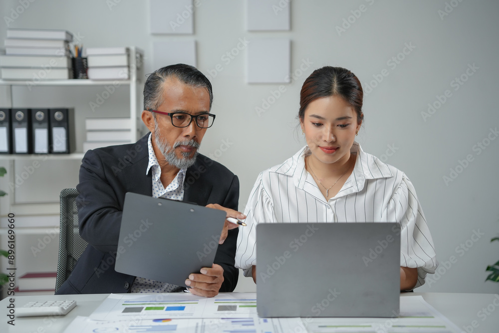 Seasoned supervisor sharing a document with a new intern and pointing to something on a laptop screen Seasoned supervisor sharing a document with a new intern and pointing to something on a laptop screen