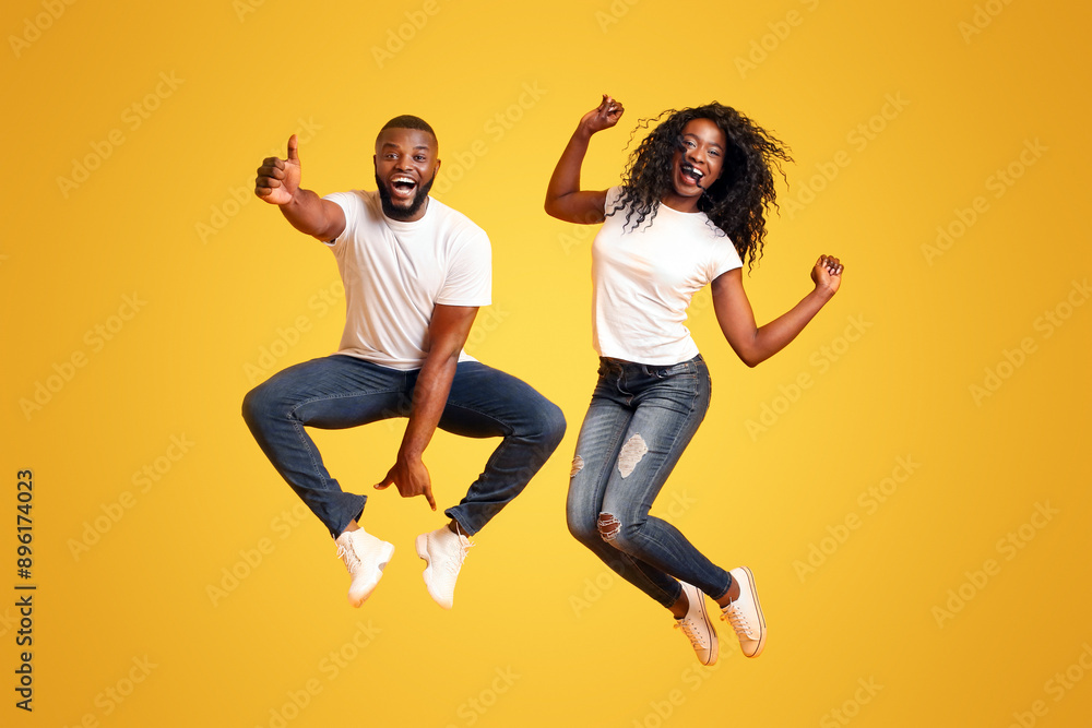 African American Young Couple Having Fun, jumping in the air, guy showing thumb up, yellow studio background African American Young Couple Having Fun, jumping in the air, guy showing thumb up, yellow studio background