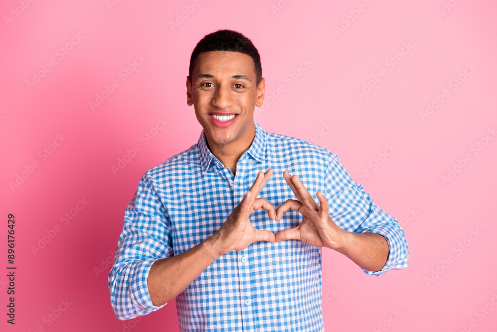 Photo of cheerful positive guy dressed checkered shirt showing heart symbol emtpy space isolated pink color background Photo of cheerful positive guy dressed checkered shirt showing heart symbol emtpy space isolated pink color background