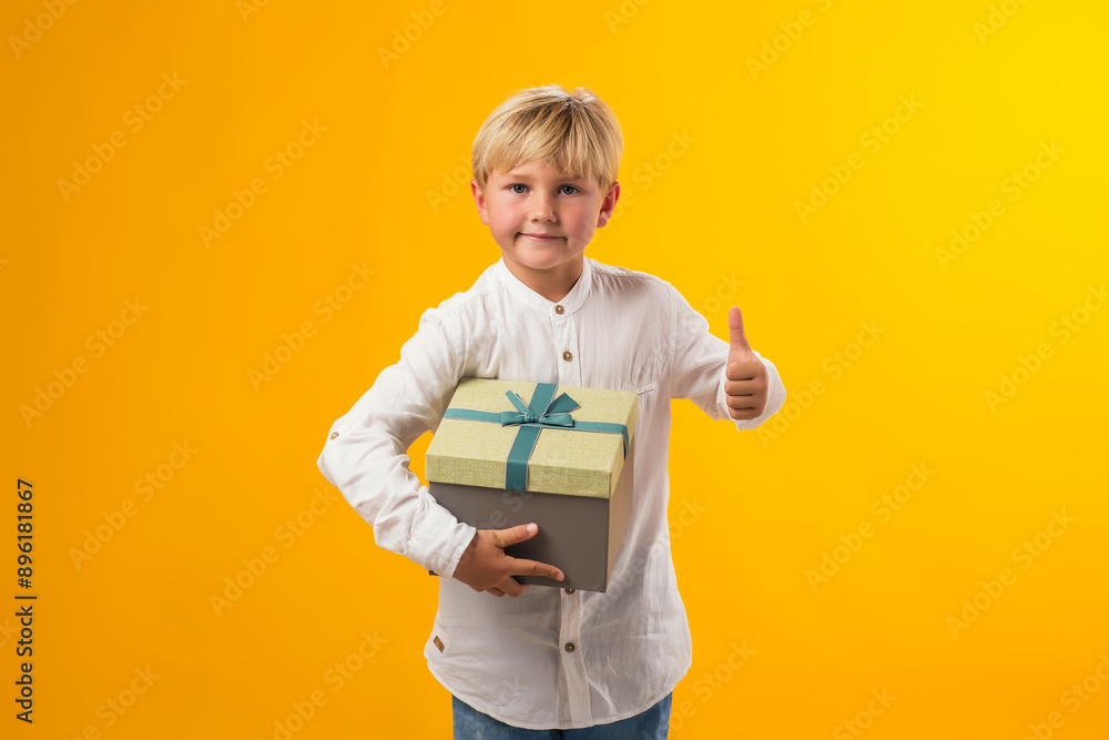 Child boy holding giftbox and showing thumb up gesture over yellow background. Birthday and celebration concept Child boy holding giftbox and showing thumb up gesture over yellow background. Birthday and celebration concept