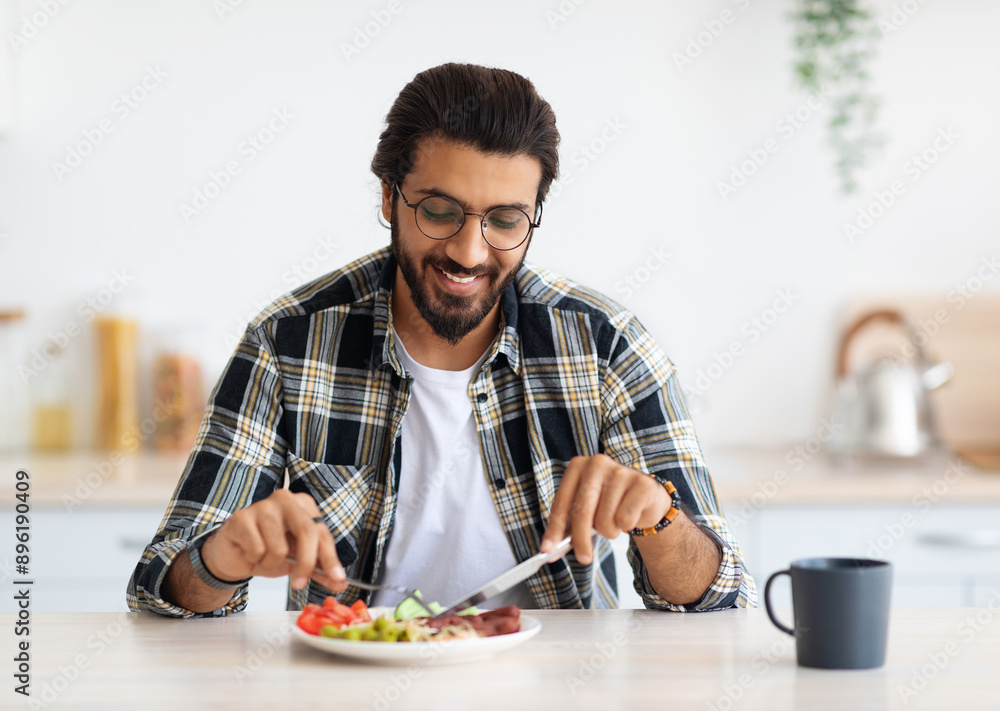 Positive arab guy hipster having healthy breakfast at home, eating fresh vegetables, sausages, drinking coffee, sitting at kitchen table, copy space. Handsome indian man starting day with nice meal Positive arab guy hipster having healthy breakfast at home, eating fresh vegetables, sausages, drinking coffee, sitting at kitchen table, copy space. Handsome indian man starting day with nice meal