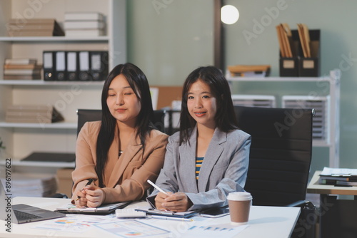 Two young Asian business woman talk, consult, discuss working with new startup project idea presentation analyze plan marketing and investment in the office.