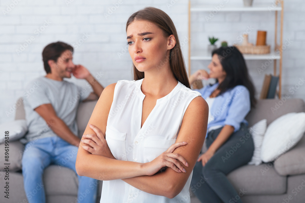 Jealousy Concept. Offended Girlfriend Standing Crossing Hands While Her Boyfriend Flirting With Girl Sitting On Sofa Indoor. Shallow Depth Jealousy Concept. Offended Girlfriend Standing Crossing Hands While Her Boyfriend Flirting With Girl Sitting On Sofa Indoor. Shallow Depth